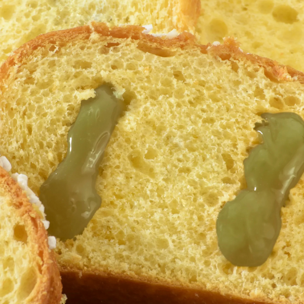 Close-up of a slice of bread with green jelly on a white background